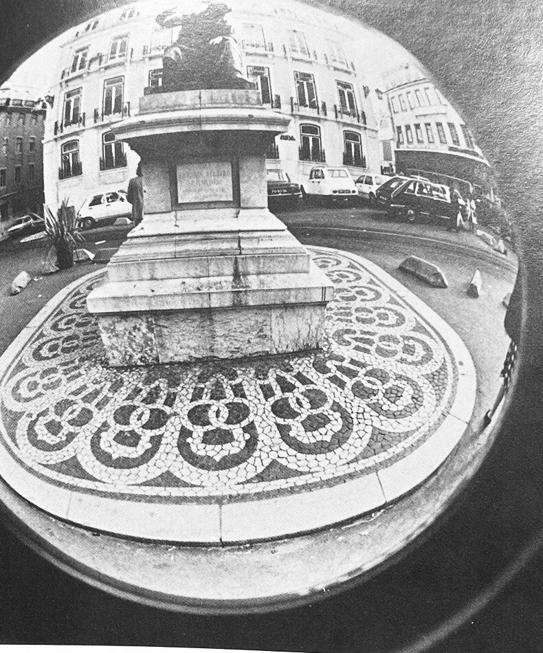Fisheye photograph of the monument to the poet Chiado standing on its patterned mosaic pavement.